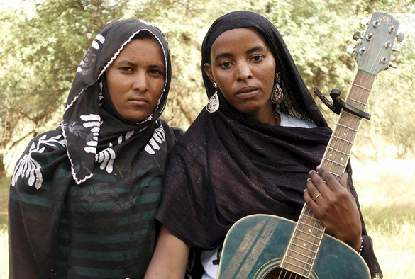 the duo outside, with one of them holding a blue/green guitar.