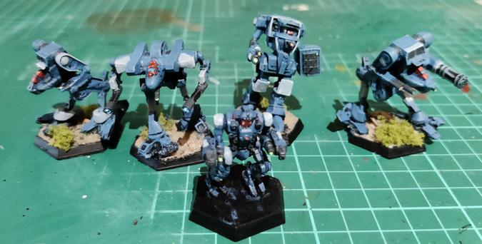 A Star of five OmniMech miniatures being painted in a Clan Diamond Shark's Lambda Spina Galaxy scheme of blue and silver, without using metallic paints. Cockpit viewports are done in red, and the energy weapons are jeweled accordingly.

The four IWM minis in line in the background - Stormcrow Prime, Cougar B, Ice Ferret E, and a Stormcorw C - are repainted Jade Falcons, so they have bases set already. The middle-front mini - a Piranha Prime - is the only plastic one by CGL, and its base is currently flat black.
