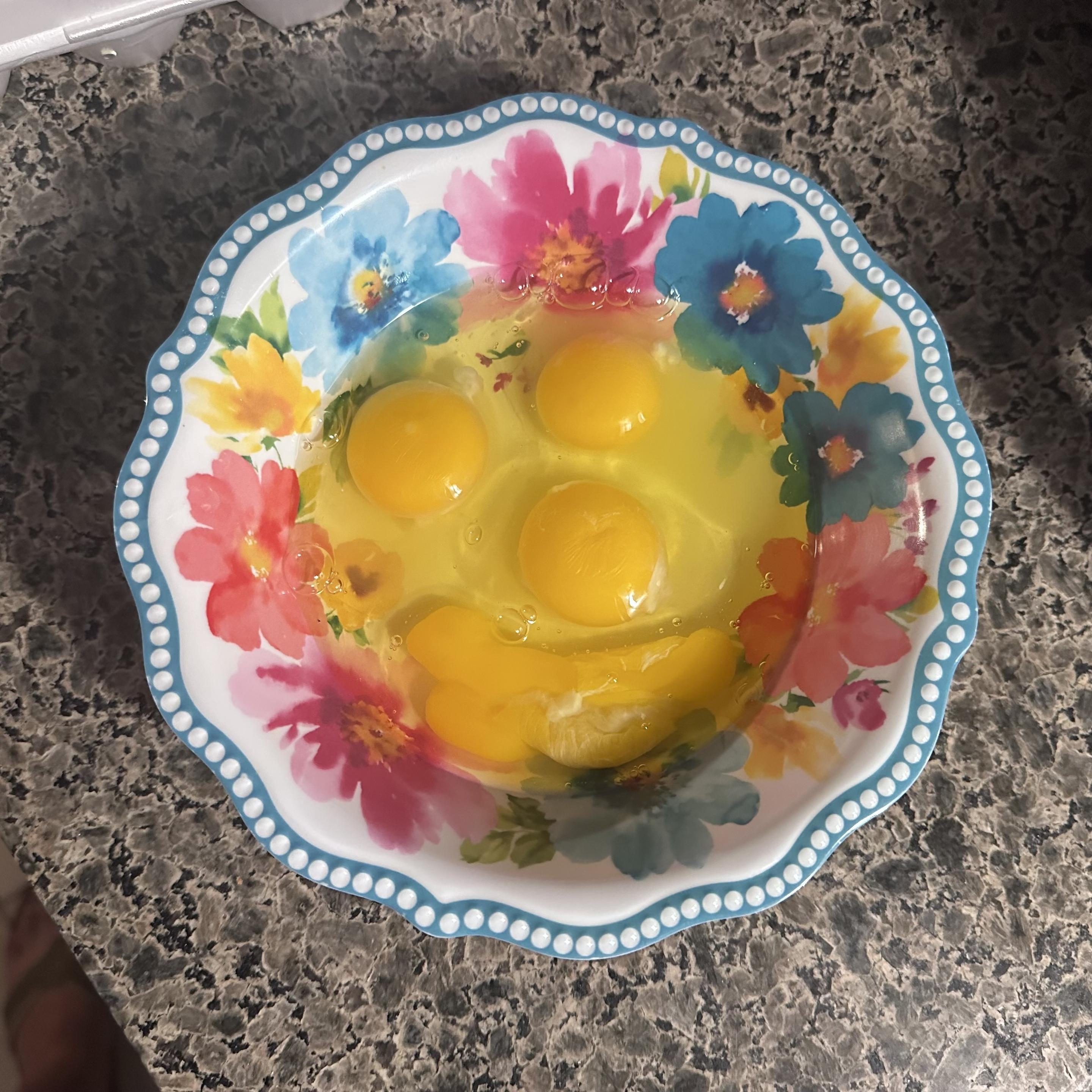 4 raw eggs in a bowl. The egg yolks make up a smiley face 