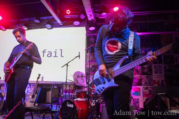 Anuj Arora playing bass on the right. Pavan Rajam playing electric guitar on the left. Both in front of a slide with word ‘fail’ showing. Photo by Adam Tow.