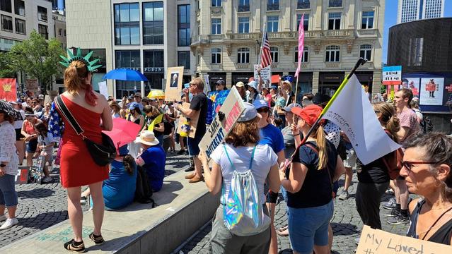 People protesting and holding signs. Some are standing in a low wall. 