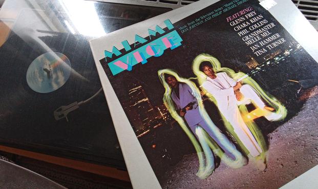pic of the Miami Vice show’s official soundtrack album, featuring the likes of Tina Turner, Grandmaster Melie Mel, Chaka Khan, Phil Collins, Glen Frey and Jan Hammer

the album art is the images of Don John & Michael Thomas, highlighted with neon lights, wearing their signature Giorgio Armanis and leather slip-ons (worn without socks), looking fetching whilst holding their guns and leaning on a black sports car
