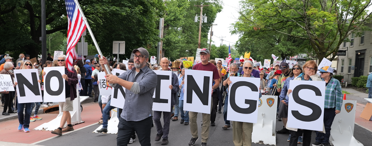 A large crowd led by flag bearer await the start of the NO KINGS parade in Kingston, NY