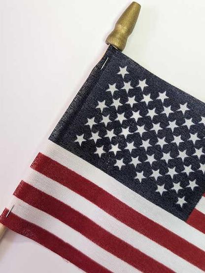 A 15x10cm tiny American flag stapled to a wooden dowel with a gold-colored wooden finial on a white background. More nicely finished versions of this product, sewn around the dowel rather than stapled to it unevenly, were eight cents per item on Alibaba.

Tiny American flags always remind me of the Tree House of Horror bit where Kang and Kodos are running for president. "Abortions for some, miniature American flags for others!"