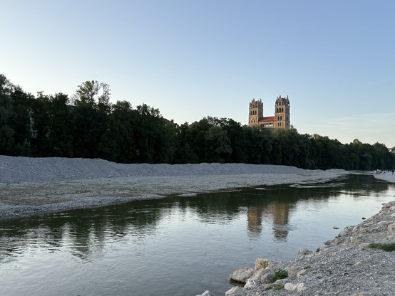 Im Fluss spiegeln sich zwei Kirchtürme, davor Bäume