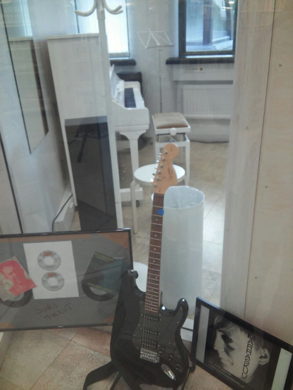 Se ve una sala con un piano y una guitarra eléctrica negra