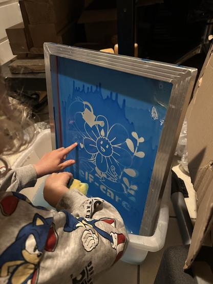 My son rinsing the screen with water and sponge to remove the unhardened emulsion, leaving our design on the screen.