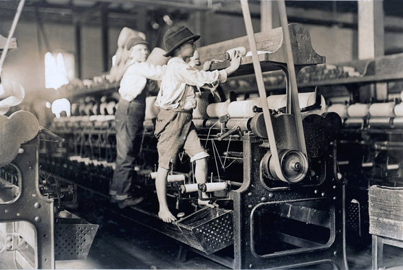 Small children climb up atop large spinning machines to mend broken threads in a Georgia cotton mill, 1909