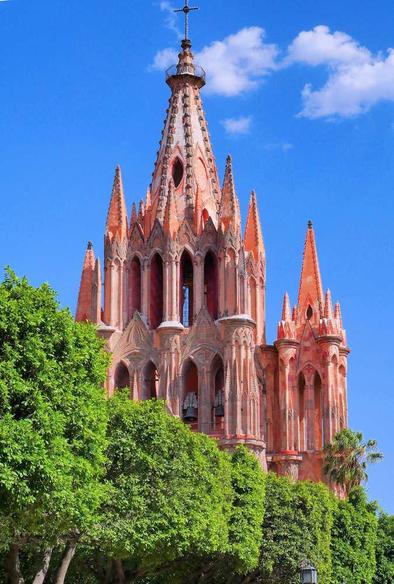 Top spires of La Parroquia de San Miguel Arcángel in San Miguel de Allende, Mexico, with green trees in the foreground