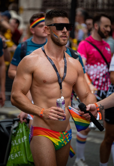 A muscular man wearing rainbow coloured speedos is walking with others during a Pride march