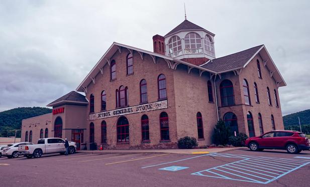 Deveral cars surround a building with an octagonal top and large windows with red trim and a sign that says DANDY and a faded WYSOX GENRAL STORE