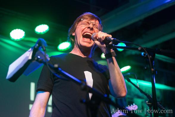 Jonathan Penn on stage, singing into a microphone with a very dramatic expression on his face. Photo by Adam Tow.
