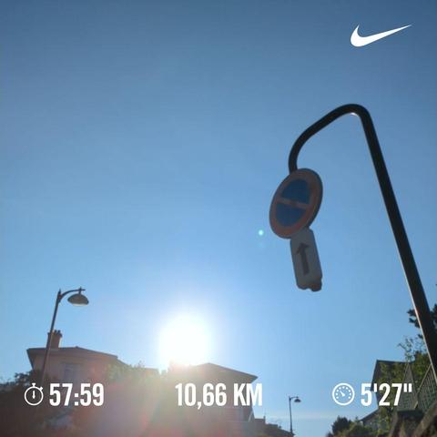 A photo of a lamppost, the Sun, and road sign (No parking) on a clear blue sky during sunset.