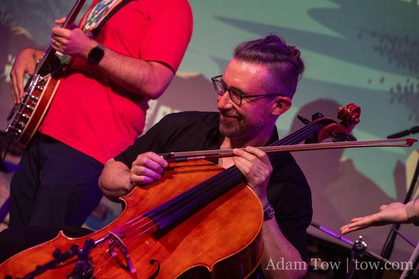 Ken Ferry in three-quarter profile, smiling, holding his cello and bow. Photo by Adam Tow.