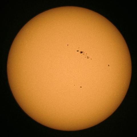 A close-up image of the Sun, predominantly orange with several sunspots visible on its surface.