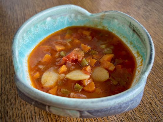 A handmade, turquoise blue ceramic bowl, filled with tomato-red soup, with vegetables and huge white Lima beans.