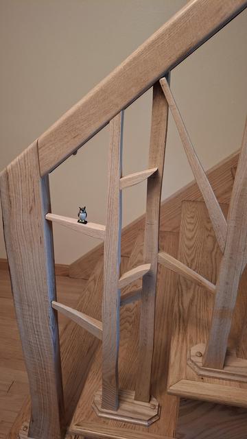 A wider look at custom oak banister resembling trees with an owl on a limb.