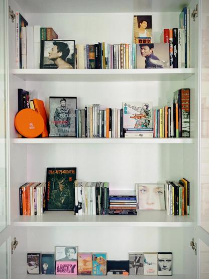 A white bookshelf showcasing a diverse collection of CDs, DVDs and cassette tapes, neatly organized across four shelves. Top shelf is my Andy Lau collection, second shelf is CantoPop and MandoPop, third shelf is American and European music, forth shelf contains only cassette tapes.