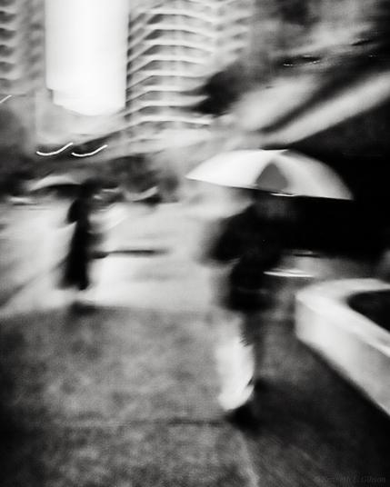 ICM image of people with umbrellas in urban area.