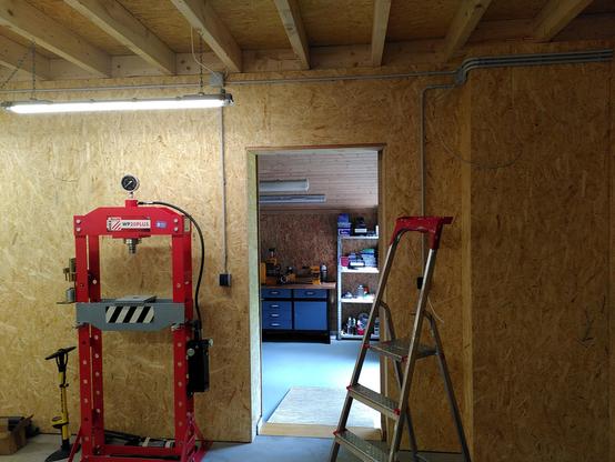 In the picture is a portal to a different workshop. To the left is a red 20 ton hydraulic press. To the right a ladder. The rooms are joined with a ramp.