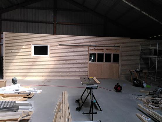 A picture of a wooden structure with a spaced slat exterior cladding. The structure has a large sliding door with 4 windows in the middle.