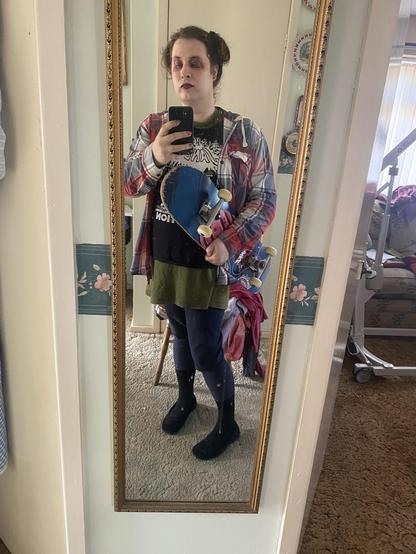 Me wearing a red plaid shirt, black T shirt, jorts and Pom Pom slippers with my skateboard.