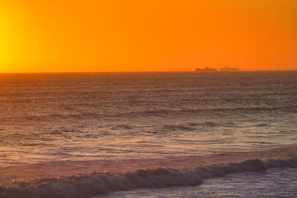 An image of sunset with two ships in the distance at horizon, orange sky and incoming waves at Bridgewater Bay Melbourne
