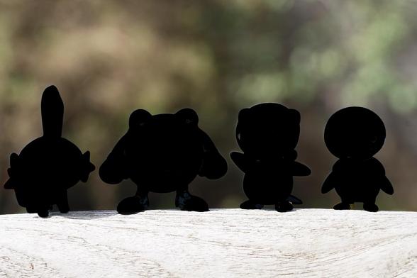 Silhouette of four toy figures of various Pokemon, positioned against a blurred natural background.