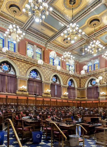 Inside the House of Representatives chambers, including stained glass windows, artfully painted walls, and rich woods.