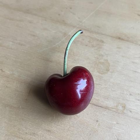 Eine einzelne dunkelrote Kirsche mit Stiel auf einem Holztisch.