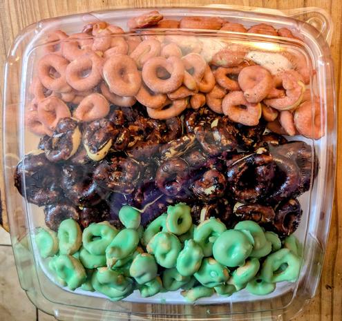 A square serving plate covered in small irregular toroidal cooked (tarallucci) frosted in red, dark chocolate, and green, arranged in horizontal bands in the style of the pan-african tricolor flag