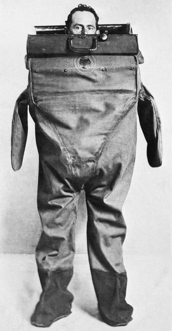 Hombre con un traje de buzo, sacando la cabeza por el maletín. Este se cierra y permite ver por una ventana redonda.