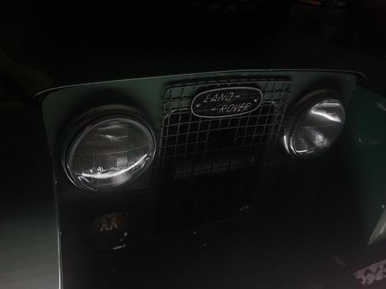 The front end of a Series Land Rover catching the last of the light as the garage door closes.
