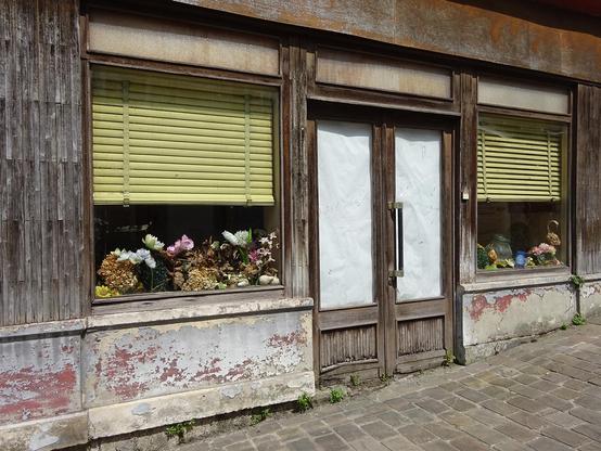 une vitrine abandonnée avec des fleurs séchées et des stores jaunes