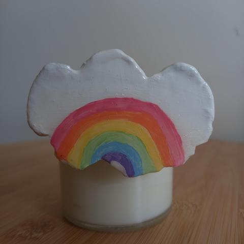 Foto a un imán con forma de nube con el arcoriris pintado (con los colores de la bandera clásica LGTBIAQ+) pegado a la parte metálica de un recipiente cilíndrico.