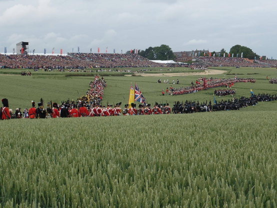 British troops march into position through the fields with bleachers for spectators stretching away in the distance