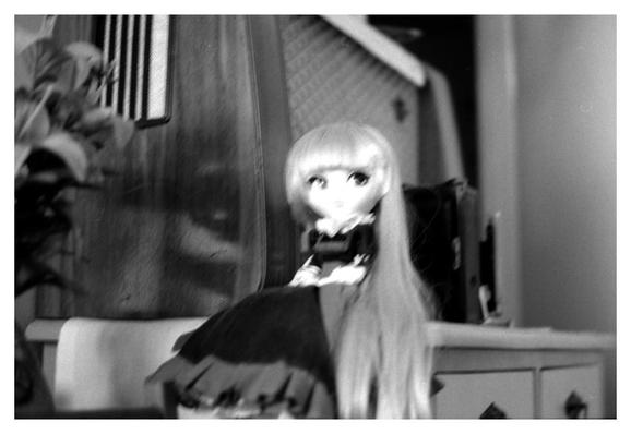An off-focus photo of Victorique de Blois ("Gosick") doll sitting on the edge of a chest of drawers, an old ASA tube radio on the background.