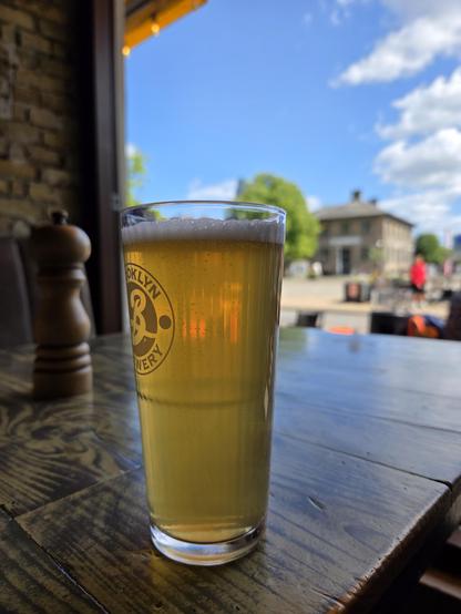 Ett ölglas i förgrunden, bakgrunden är ett solbelyst torg. 