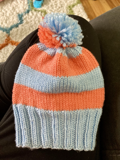 A light orange and light blue striped hand-knit beanie
