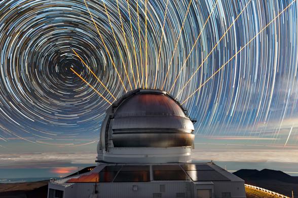 Laser light and star trails combine for a cosmic light show at Gemini North, one half of the International Gemini Observatory which is supported in part by the U.S. National Science Foundation and operated by NSF NOIRLab, on Maunakea in Hawai‘i. This scene was created by combining multiple timelapse images. 

In the foreground sits Gemini North, situated near the highest point in the Pacific Basin at an altitude of 4213 meters (13,822 feet). The orange streaks were created by Gemini’s Laser Guide Star (LGS) system at several different observing positions. The laser creates an ‘artificial star’ by interacting with atoms in the upper atmosphere approximately 90 kilometers (50 miles) above the Earth. Earth’s atmosphere distorts light from the laser-created ‘star’, just as it distorts the light from objects under study. By measuring these distortions, Gemini’s adaptive optics system can correct for them in the telescope’s science observations, resulting in crisper, clearer views of the Universe for astronomers. 

In the background, stars swirl around Polaris, the northern hemisphere’s pole star. As Earth rotates over the course of a night, stars seem to circle the celestial poles, showing up as trails in long-exposure photographic images.