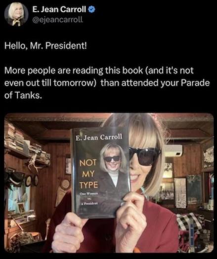 Screenshot of a post by E. Jean Carroll.  The picture is of her, in sunglasses holding up a copy of her book.  The cover is a picture of her, her name across the top and the title, Not My Type next to her photo.  Her post reads, "Hello Mr President!  More people are reading this book (and it's not even out till tomorrow) than attended your Parade of Tanks
