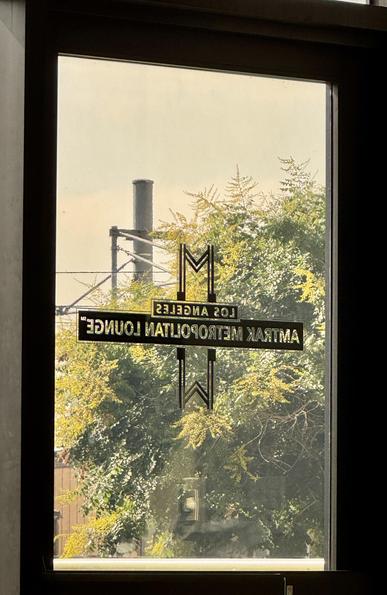 Looking out a glass door with a label that says Los Angeles Amtrak Metropolitan Lounge. Trains are running by in the background.