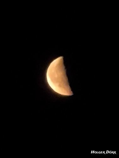 Zunehmender Mond in warmem Licht vor schwarzem Himmel. Die linke Seite ist beleuchtet. Aufnahme bei Nacht, spontan unterwegs entstanden.