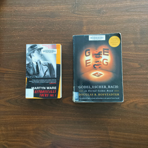 A photo of two books on a table. The book on the left is Martyn Ware's "Electronically Yours", with a photo of the author in his mid-20s on the cover, wearing a retro-styled trilby hat, raincoat, suit and tie. The book on the left is Douglas Hofstadter's "Godel, Escher and Bach", with an abstract arrangement of the letters G, E and B in a cube-like pattern.
