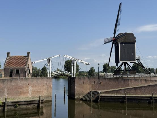 A harbour, wall of stone, with a gate bridge over the water. Windmill to the right. 