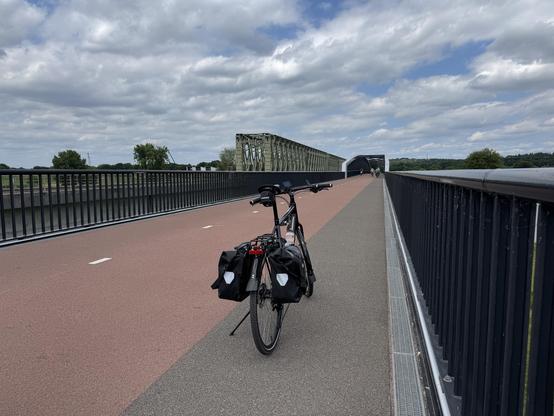 Bicycle on a bridge for cyclists, two lanes, plus a grey one for pedestrians. Another bridge to the left for trains. 