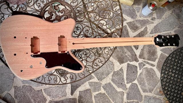 Eine E-Gitarre aus Mahagoni im Bau, reverse offset Form, von oben fotografiert, auf einem Gartentisch aus Metallornamenten liegend. Das Griffbrett und die Hardware fehlt noch. 
