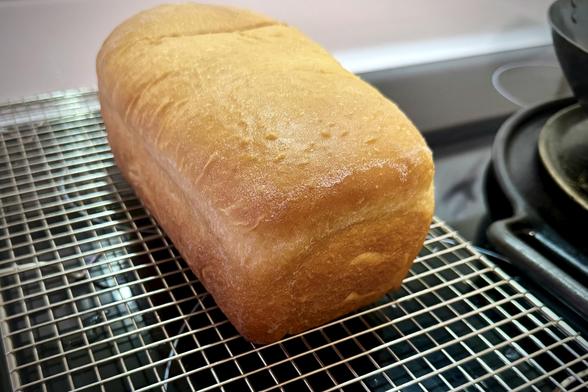 A loaf of freshly baked sandwich bread cools on a cooling rack.