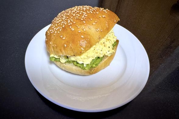 Egg salad in a sesame topped hamburger bun along with mashed and seasoned avocado.