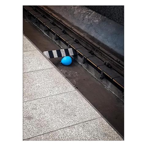 A blue balloon fell between the subway tracks and got stuck under a black and white beam.